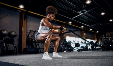 Motivated strong sporty lady performing the alternating waves exercise with battle ropes at the gym